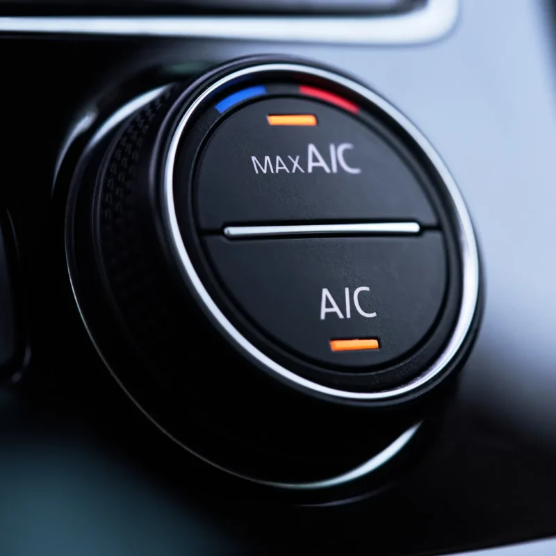 Close-up of a car's black air conditioning control knob labeled MAX A/C and A/C with orange indicator lights illuminated.